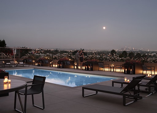 Couple standing along the outdoor pool with lounge chairs at dusk