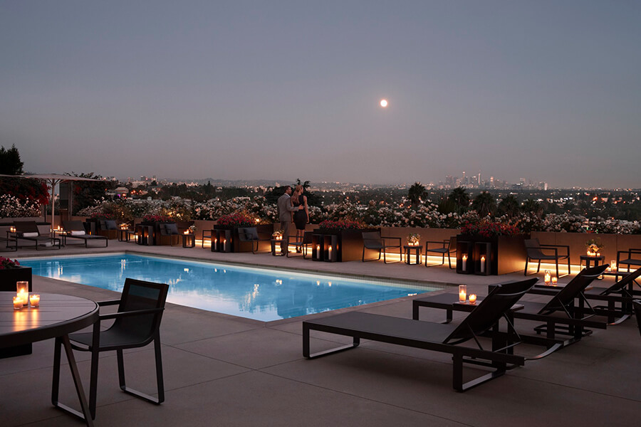 Couple standing along the outdoor pool with lounge chairs at dusk